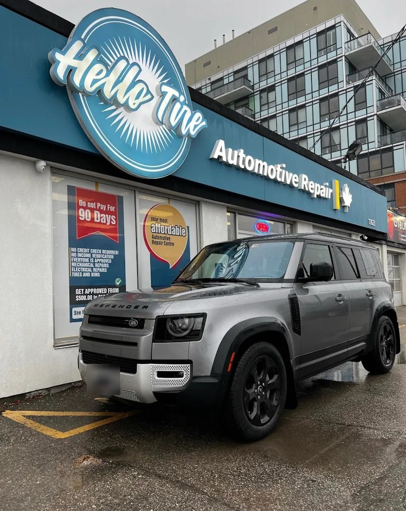 A grey Land Rover Defender parked in front of the Hello Tire sign