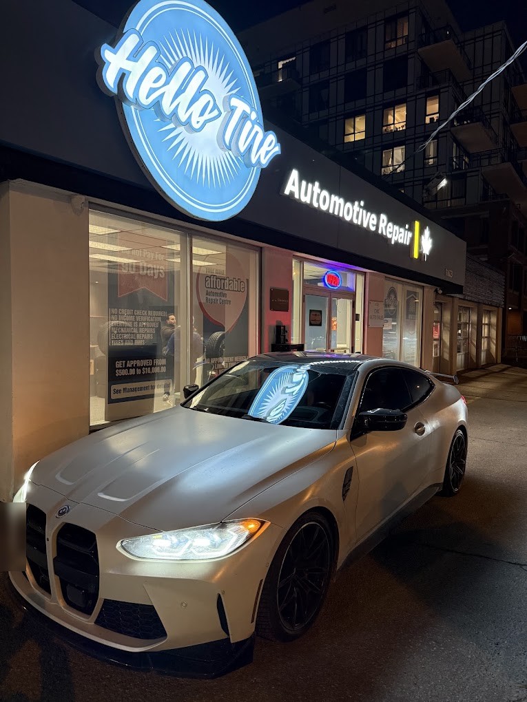 A white BMW M4 coupe parked under the lit Hello Tire sign at night