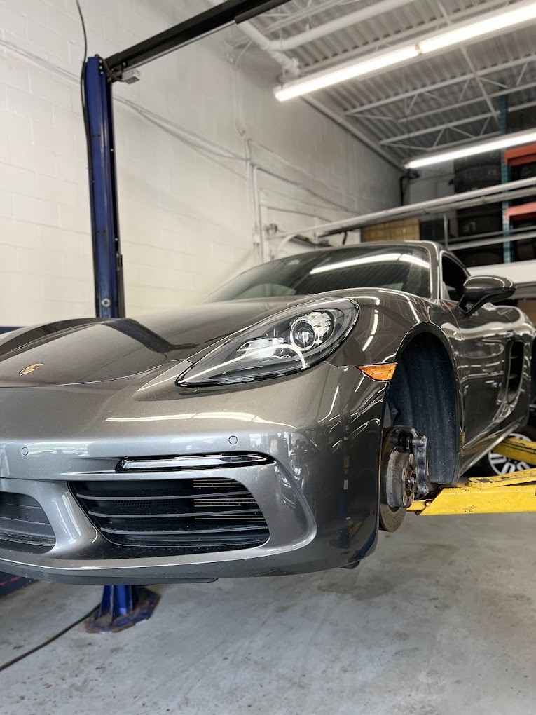 A grey Porsche Cayman on a Hello Tire lift with a front wheel off and the brake exposed