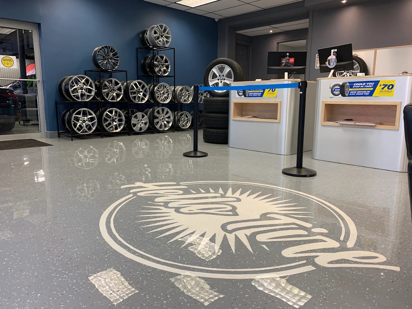 The Hello Tire showroom with the logo on the polished floor and a wall of wheels